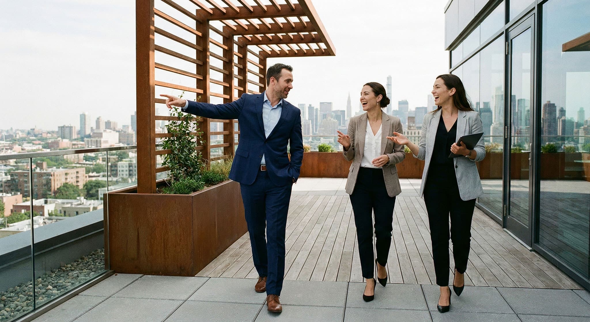 Drei Personen in Geschäftskleidung gehen und unterhalten sich auf einer modernen Dachterrasse mit der Skyline der Stadt im Hintergrund; ein Mann gestikuliert nach außen, während die beiden Frauen zuhören und lächeln, während sie über München Immobilien mit Lkm real estate diskutieren.