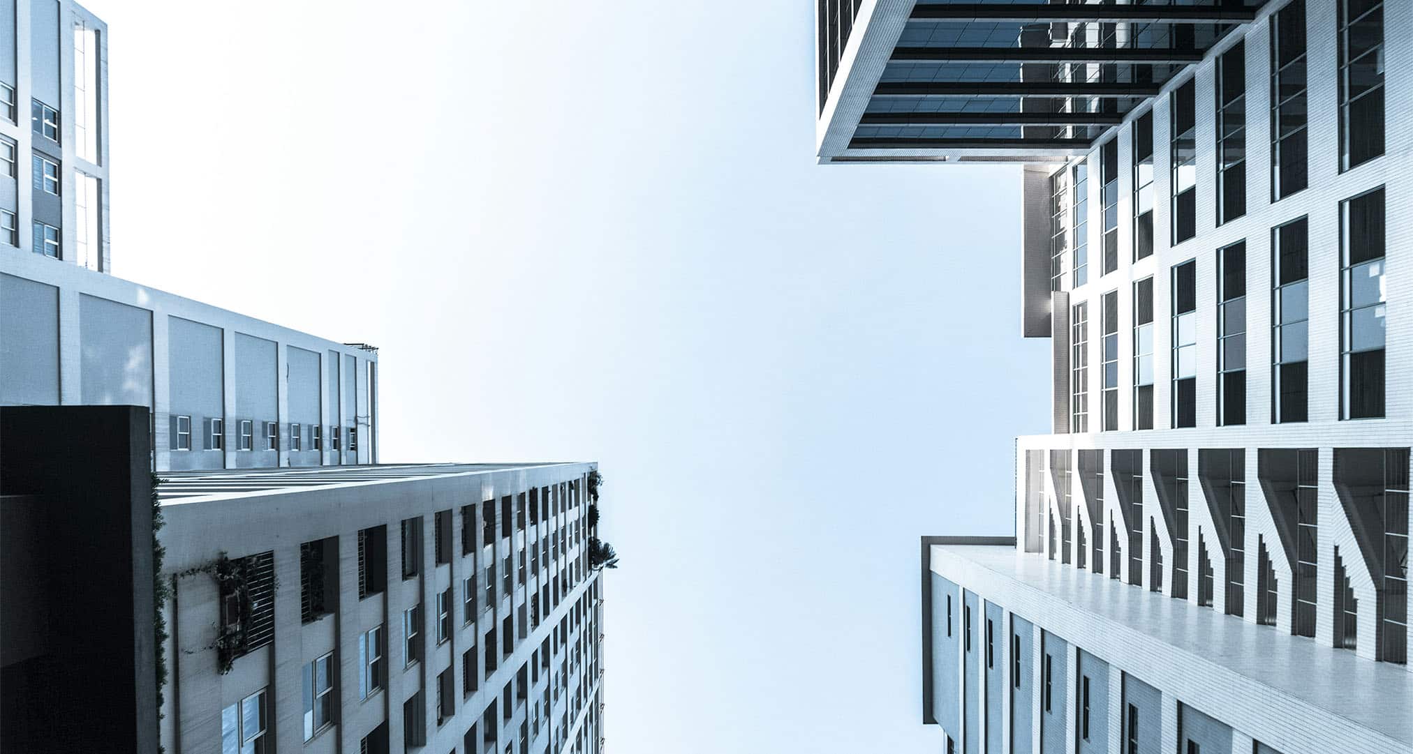 Hohe moderne Gebäude in München, fotografiert von unten, mit Blick auf den blauen Himmel zwischen den Gebäuden. Mit klaren Linien und vielen Fenstern spiegelt diese Szene den zeitgenössischen Stil von Lkm-Immobilien und innovativem Immobilien-Design wider.